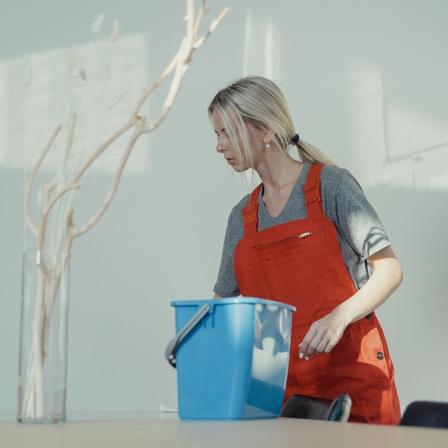 Cleaner in a red apron with a blue bucket in a bright room